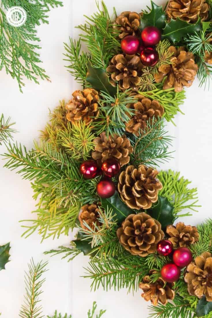 Handmade wreaths are a wonderful way to spread some holiday cheer to your loved ones. This classic red and green pinecone wreath is made with pinecones, spruce, conifer twigs, holly leaves, and red mini bauble ornaments. Check out the tutorial and get creative! #Christmas #flowerarranging #wreath | countryhillcottage.com Handmade wreaths are a wonderful way to spread some holiday cheer to your loved ones. This classic red and green pinecone wreath is made with pinecones, spruce, conifer twigs, holly leaves, and red mini bauble ornaments. Check out the tutorial and get creative! #Christmas #flowerarranging #wreath | countryhillcottage.com