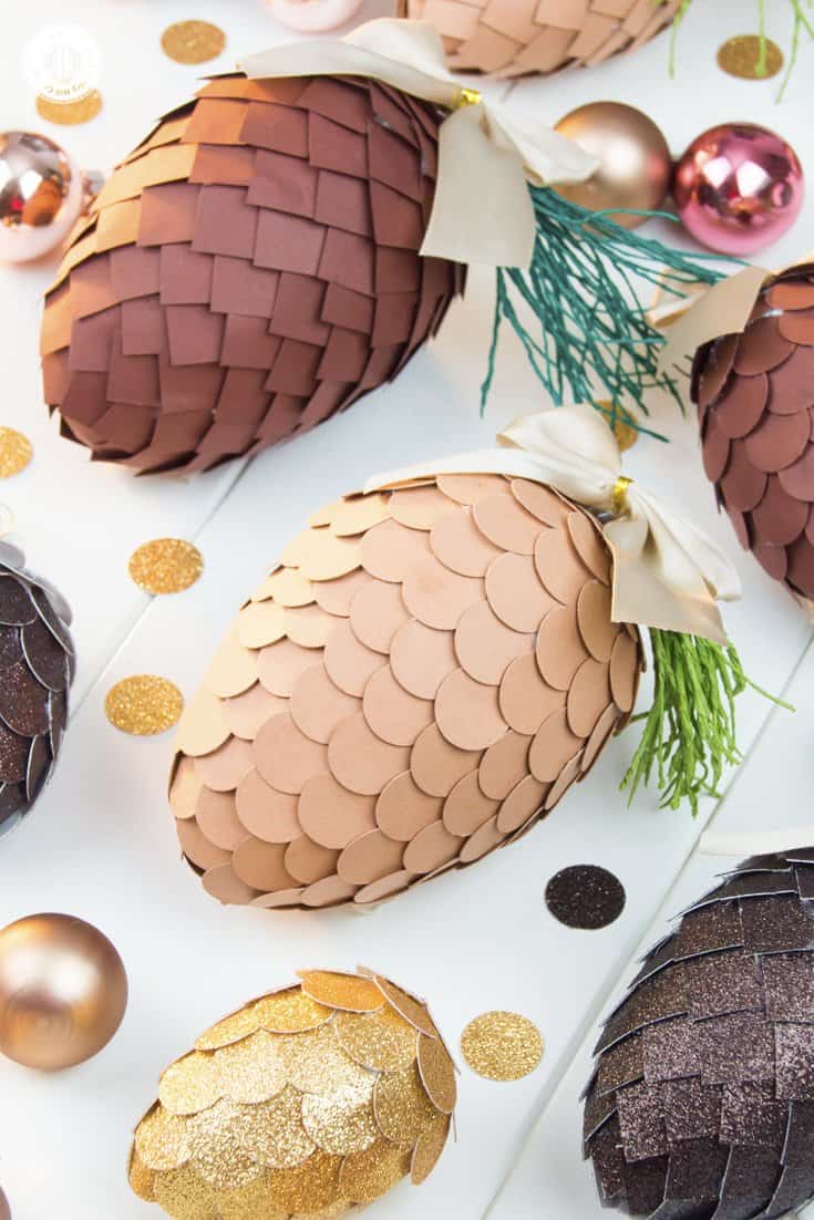 Learn how to make paper pinecone ornaments that you can use to decorate your Christmas tree or for packaging gifts. The ornaments are made by applying small paper squares or circles on polystyrene eggs. You can choose any size of egg shape and use a wide variety of papers for the scales, such as cardstock, scrapbook paper, glitter paper, or gift wrap. We also demonstrate how to make pine needles form crepe paper to decorate the ornaments. #DIY #pinecone #papercrafts | countryhillcottage.com
