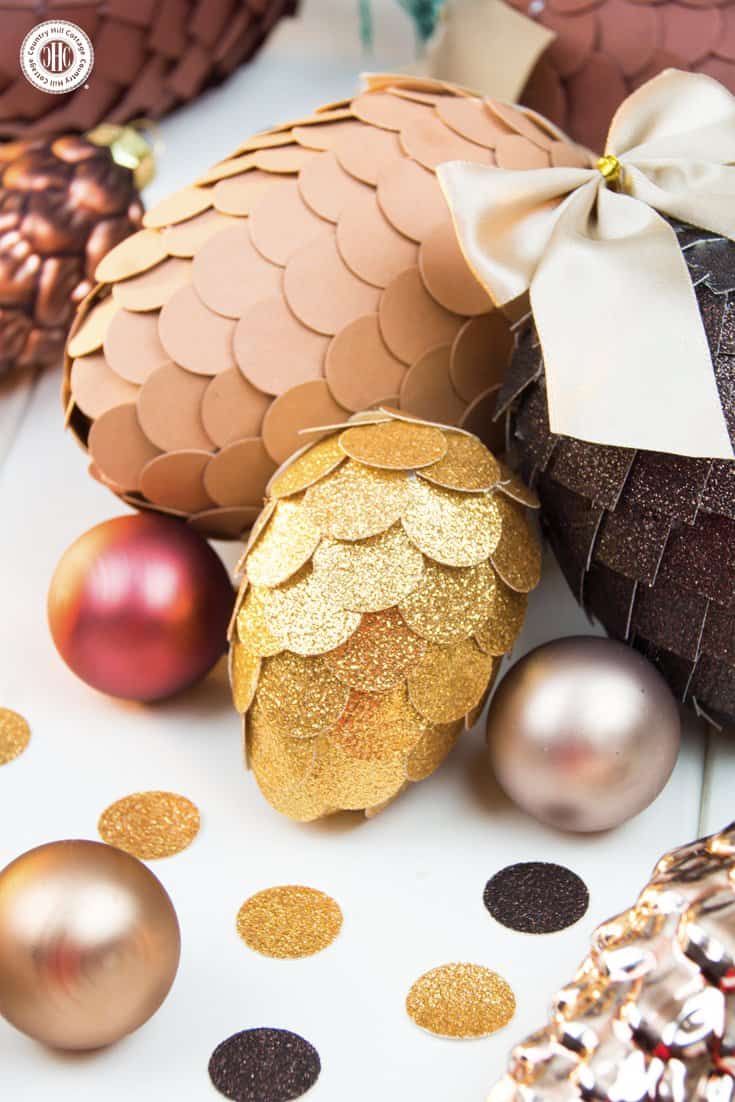 Learn how to make paper pinecone ornaments that you can use to decorate your Christmas tree or for packaging gifts. The ornaments are made by applying small paper squares or circles on polystyrene eggs. You can choose any size of egg shape and use a wide variety of papers for the scales, such as cardstock, scrapbook paper, glitter paper, or gift wrap. We also demonstrate how to make pine needles form crepe paper to decorate the ornaments. #DIY #pinecone #papercrafts | countryhillcottage.com