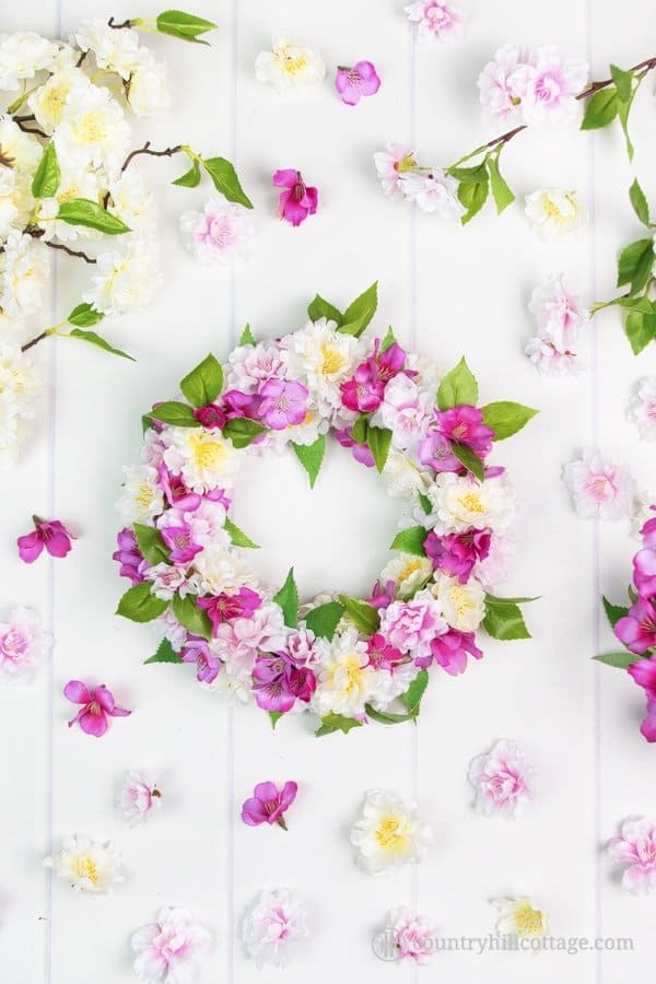 A tutorial on how to create a stunning DIY silk flower wreath with spring blossoms. Fire up your hot glue gun, grab yourself a wreath form and a bunch of silk blossoms and craft yourself to spring galore. This adorable faux flower wreath brings instant spring flair to your home and lasts season after season. You can use the blossom wreath to brighten up your front door, use it as a table topper, or give it to a friend. #silkflowers #fauxflowers #wreath #blossomwreath | countryhillcottage.com A tutorial on how to create a stunning DIY silk flower wreath with spring blossoms. Fire up your hot glue gun, grab yourself a wreath form and a bunch of silk blossoms and craft yourself to spring galore. This adorable faux flower wreath brings instant spring flair to your home and lasts season after season. You can use the blossom wreath to brighten up your front door, use it as a table topper, or give it to a friend. #silkflowers #fauxflowers #wreath #blossomwreath | countryhillcottage.com