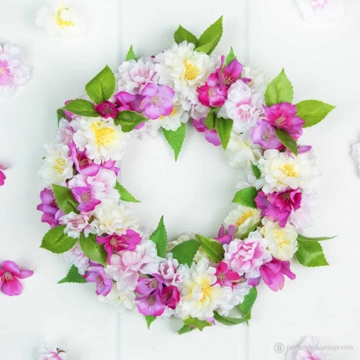 A tutorial on how to create a stunning DIY silk flower wreath with spring blossoms. Fire up your hot glue gun, grab yourself a wreath form and a bunch of silk blossoms and craft yourself to spring galore. This adorable faux flower wreath brings instant spring flair to your home and lasts season after season. You can use the blossom wreath to brighten up your front door, use it as a table topper, or give it to a friend. #silkflowers #fauxflowers #wreath #blossomwreath | countryhillcottage.com