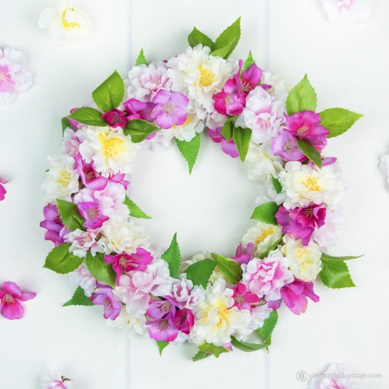 A tutorial on how to create a stunning DIY silk flower wreath with spring blossoms. Fire up your hot glue gun, grab yourself a wreath form and a bunch of silk blossoms and craft yourself to spring galore. This adorable faux flower wreath brings instant spring flair to your home and lasts season after season. You can use the blossom wreath to brighten up your front door, use it as a table topper, or give it to a friend. #silkflowers #fauxflowers #wreath #blossomwreath | countryhillcottage.com