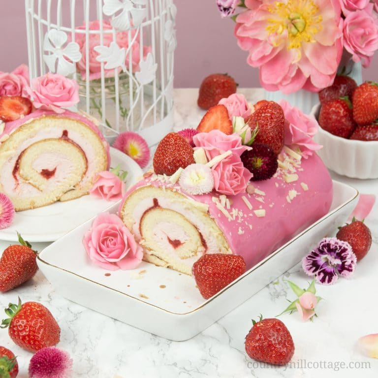 This easy strawberry roll cake recipe features soft sponge cake, a fluffy strawberry cream cheese and whipped cream filling, enrobed by shiny mirror glaze and with fresh berries and flowers as decoration. Whether you call this tasty dessert strawberry cake roll, strawberry Swiss roll, or strawberry roulade, this sweet treat tastes delicious and is perfect for entertaining guests. Strawberry Swiss Roll | Strawberry Roulade #strawberry #rollcake #swissroll #mirrorglaze| countryhillcottage.com