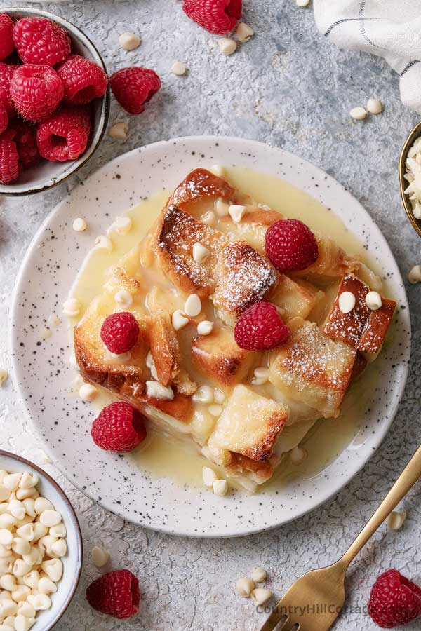 slice of white chocolate bread pudding with white chocolate sauce on a plate.