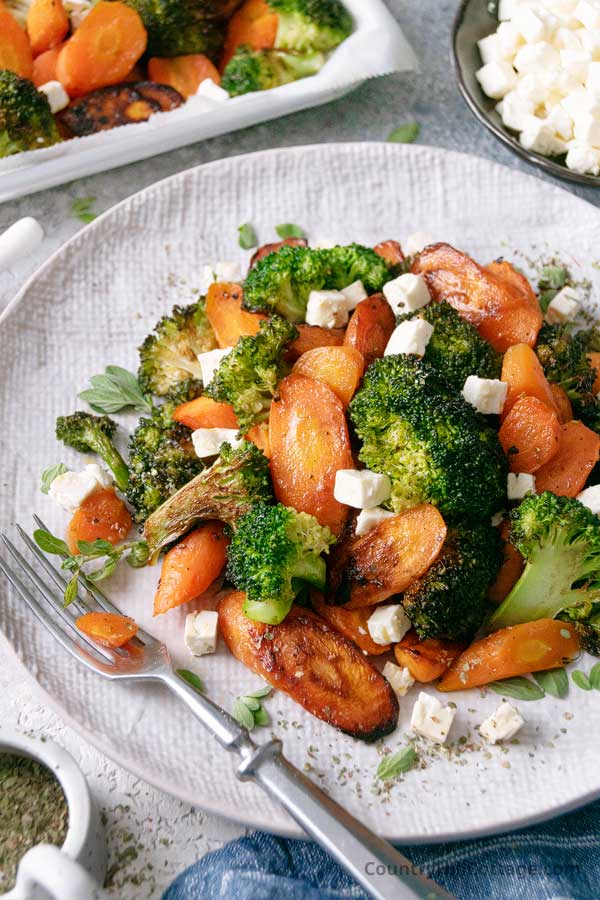 closeup of roasted broccoli and carrots on a plate with a fork.