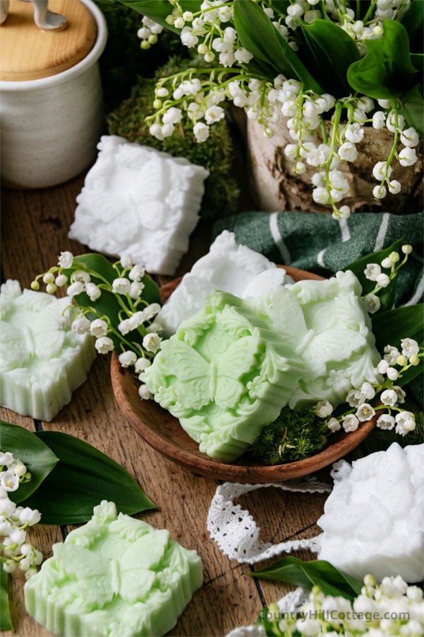 3 bars of lily of the valley soap in wooden bowl with fresh lily of the valley flowers.