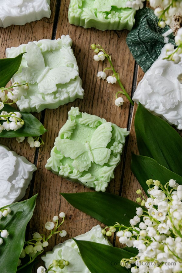 lily of the valley soap bars on a wooden table surrounded by lily of the valley flowers.
