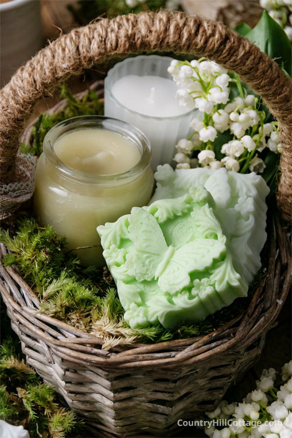 two soap bars, jar of body butter, and candle, and a small bouquet in a rustic gift basket.